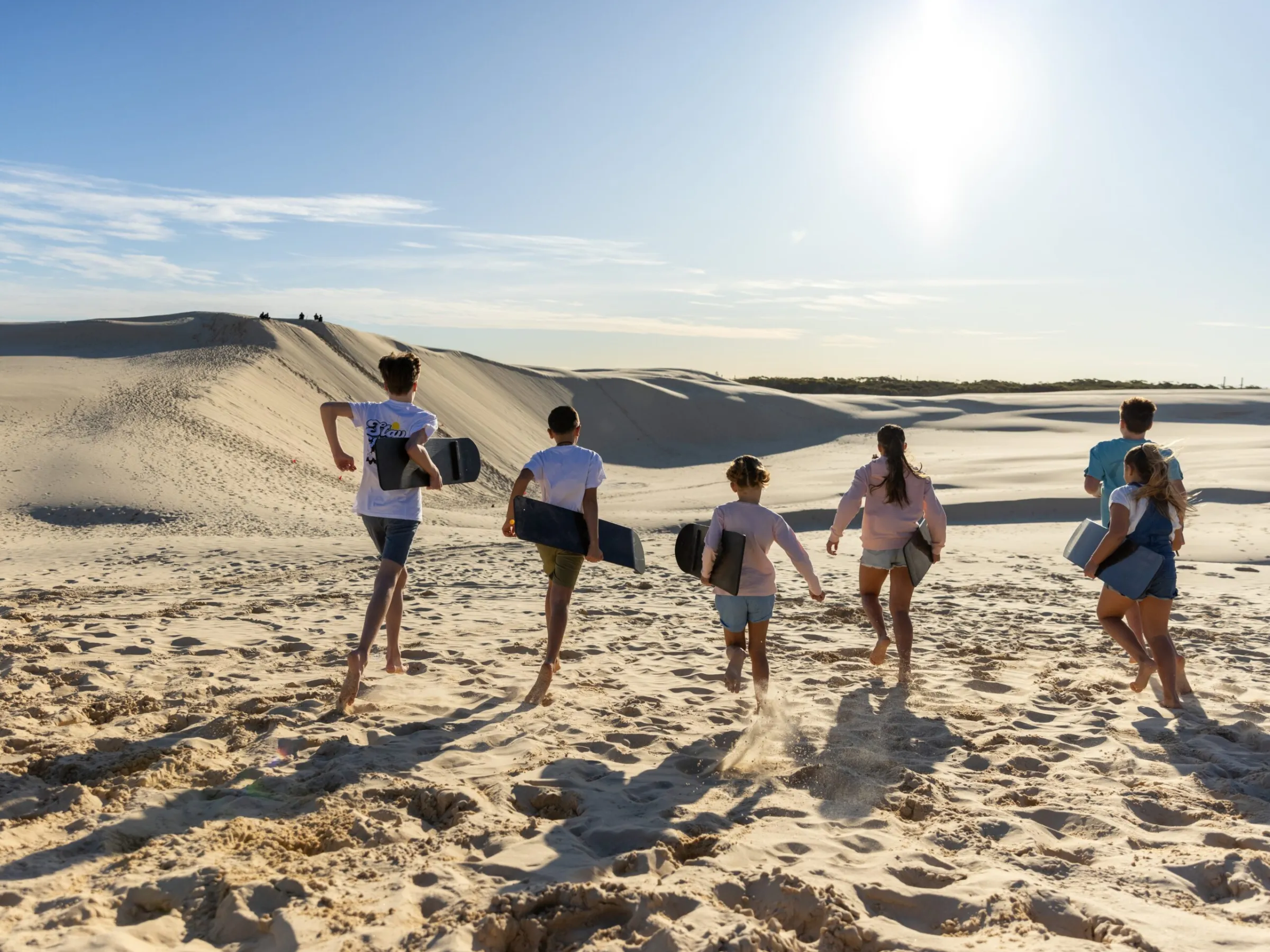 a group of people posing for the camera with their sandboards raised above their heads in anna bay, nsw