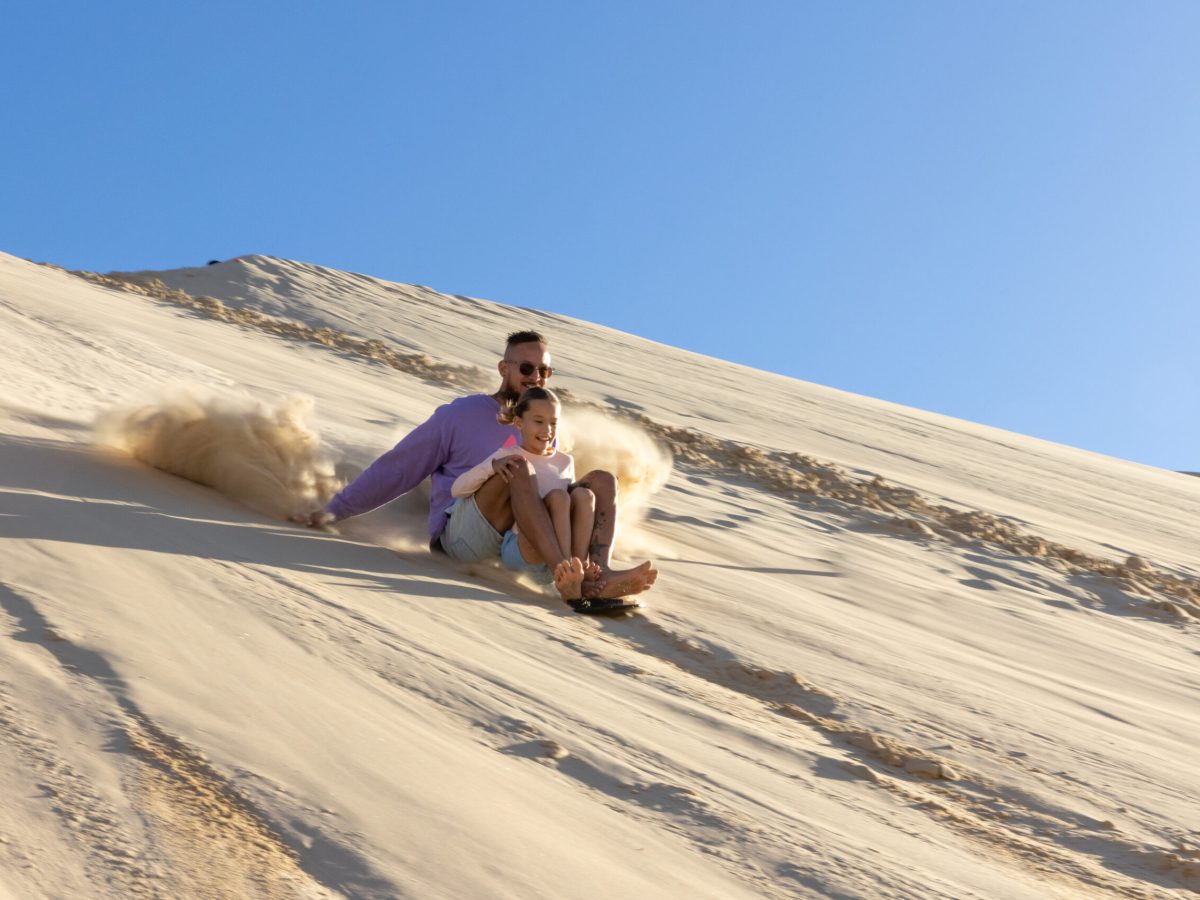 a father and daughter having fun sandboarding with 4wd tours r us in anna bay, nsw