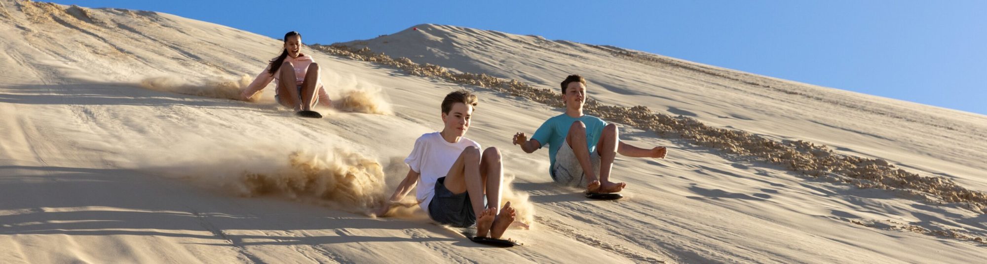a group of people sandboarding with 4wd tours r us in anna bay, nsw