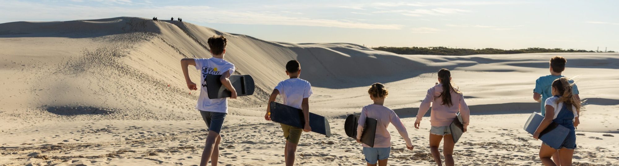 a group of people posing for the camera with their sandboards raised above their heads in anna bay, nsw
